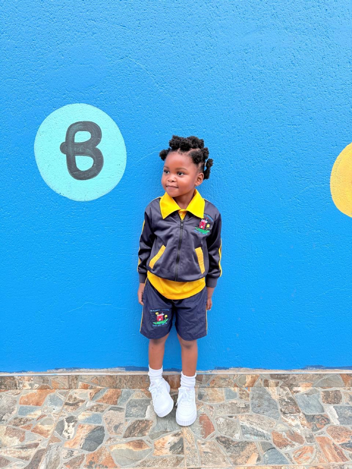 A girl in Little Champions tracksuit uniform at the painted letter wall